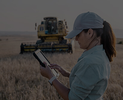 A girl with a tablet computer is standing on a crop field near a harvester.
