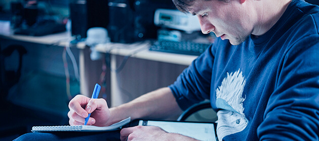 A man is sitting in an office chair and making notes. 