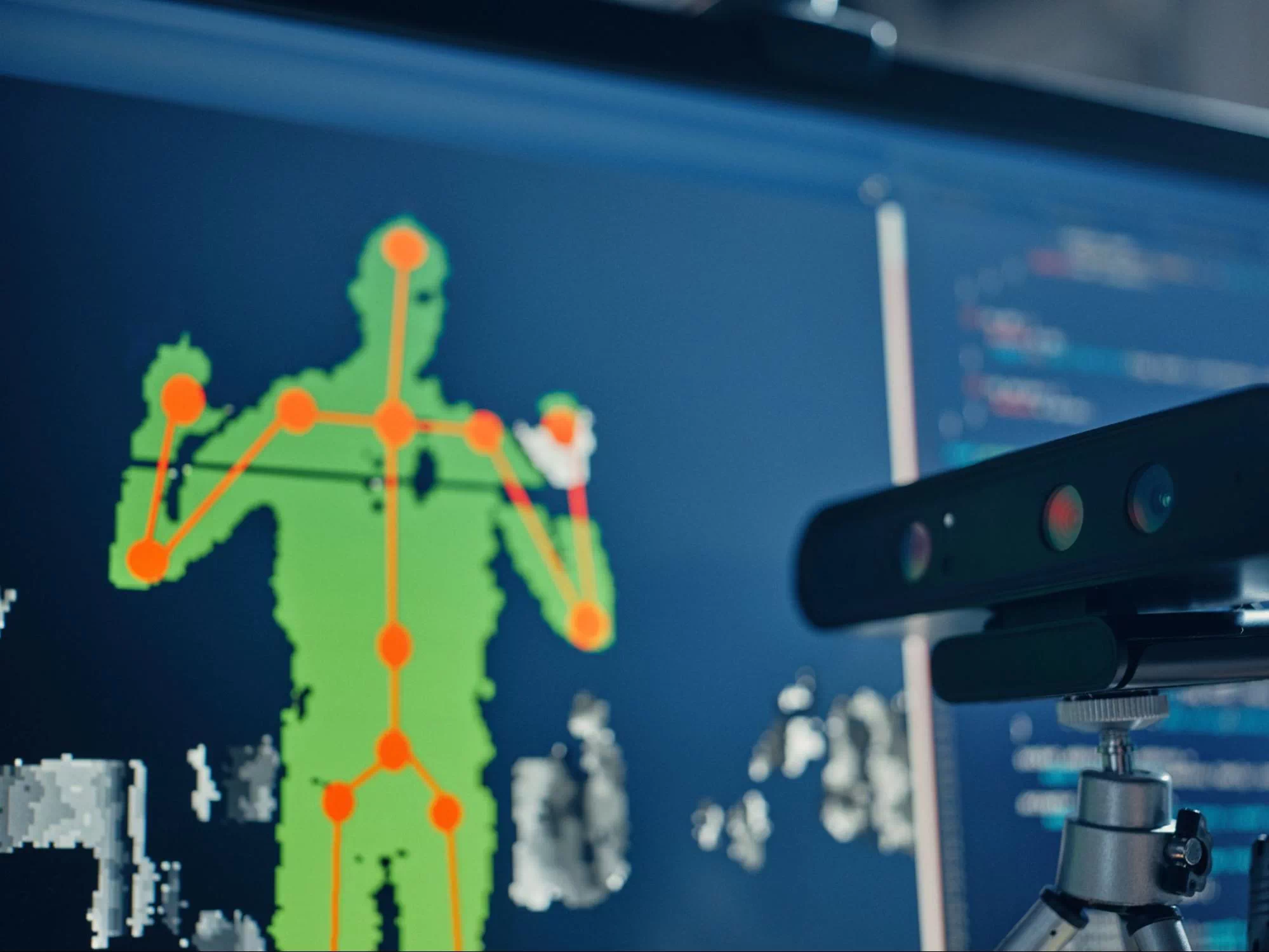 A video camera and a monitor screen behind it with an image of a human processed by a computer vision application.