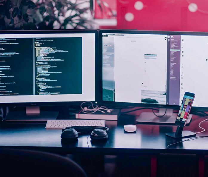 A desk with two monitors, headphones, and a smartphone holder.