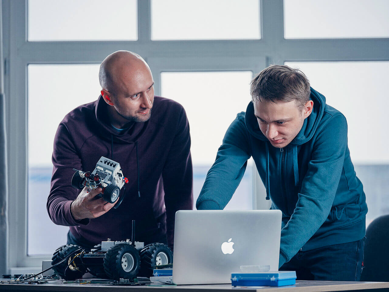 Two Integra Sources' engineers are programming a robot on a laptop.