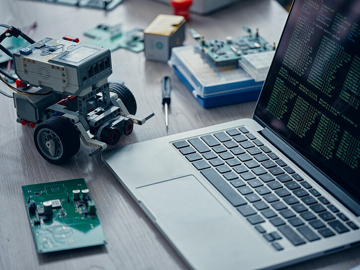 A laptop, a PCB, and a wheeled robot on a table