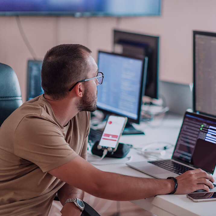 An Integra Sources engineer sits at a table filled with a monitor and laptops, setting up a mobile application on a tablet.