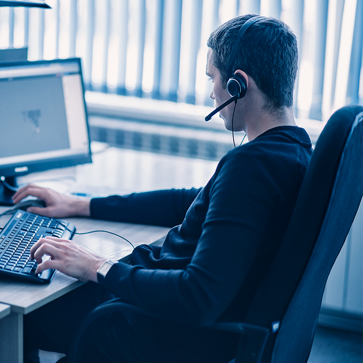 A customer service specialist is answering the phone sitting at his desk.