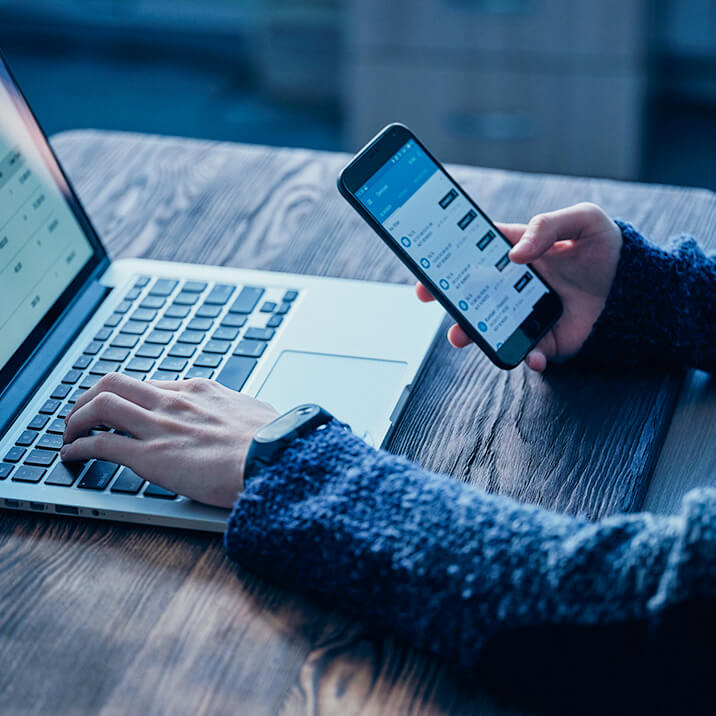 A man typing on a laptop and holding a smartphone.