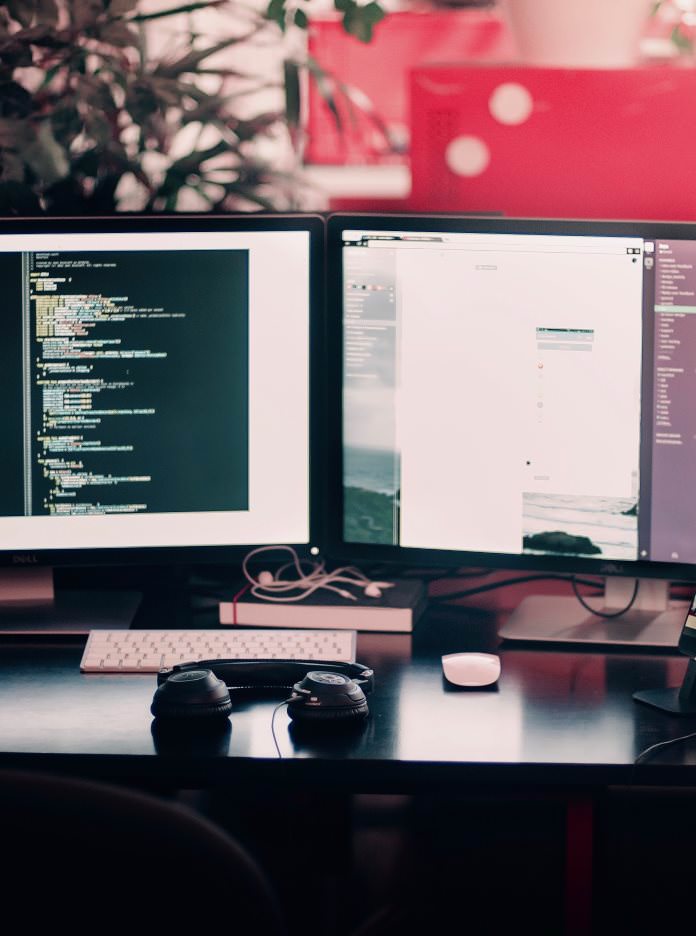 A desk with two monitors, headphones, and a smartphone holder.